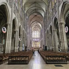 Wnętrze bazyliki Saint-Denis z rzędami drewnianych krzeseł i witrażami.