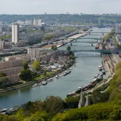 Rozległe miasto z wieloma mostami, gdzie płynie Sekwana, otoczone zielonymi wzgórzami.