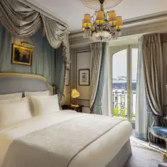 Elegancka sypialnia w hotelu Ritz Paryż. Luksusowe zasłony, baldachim nad łóżkiem i kryształowy żyrandol tworzą atmosferę królewskiego splendoru.