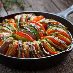 Ratatouille, jedno z popularnych dań francuskich, w naczyniu żeliwnym. Warzywa ułożone w wachlarz, ozdobione ziołami.