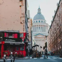 Urokliwa ulica w dzielnicy łacińskiej Paryża z czerwonym bistro i majestatycznym Panteonem w tle.