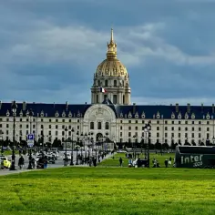 Złota kopuła Les Invalides góruje nad placem w Paryżu. Ruch uliczny i zielony trawnik tworzą tło dla tego historycznego miejsca.