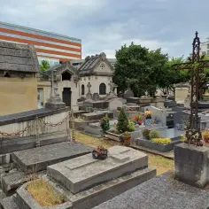 Kamienne nagrobki i mauzolea na cmentarzu w Paryżu, z nowoczesnym budynkiem w tle.