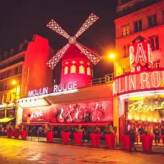 Nocny Paryż rozświetlony neonami kabaretu Moulin Rouge. Czerwony wiatrak i wejście zapraszają na wieczór pełen wrażeń.