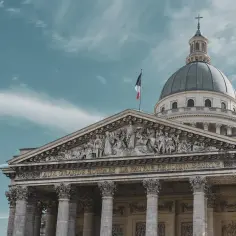 Majestatyczny Panteon w Paryżu z kopułą i francuską flagą na tle błękitnego nieba.