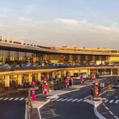 Port lotniczy Paryż-Orly Ouest w złotym świetle zachodzącego słońca. Samochody i autokary czekają na pasażerów.