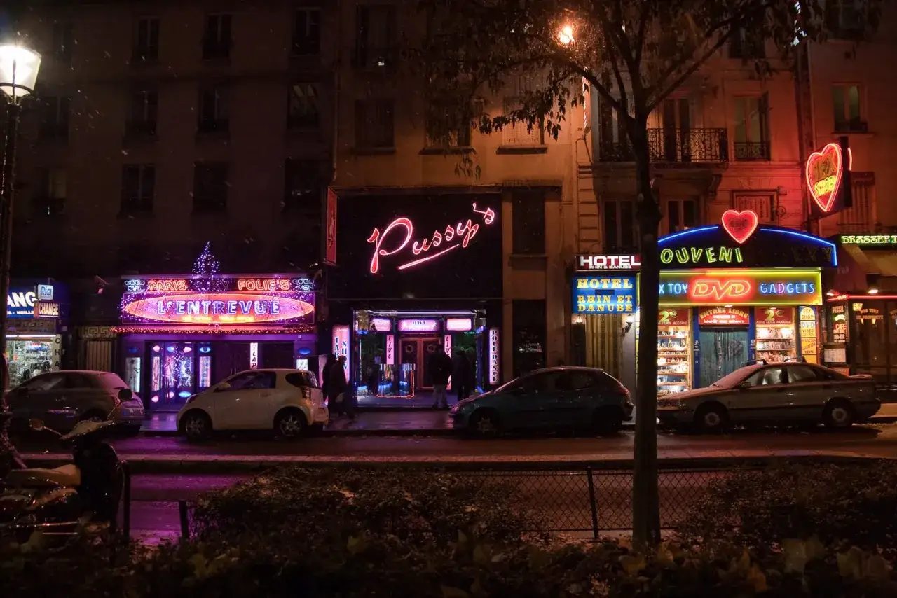 Nocne światła neonów na placu Pigalle w Paryżu, śnieg i samochody.
