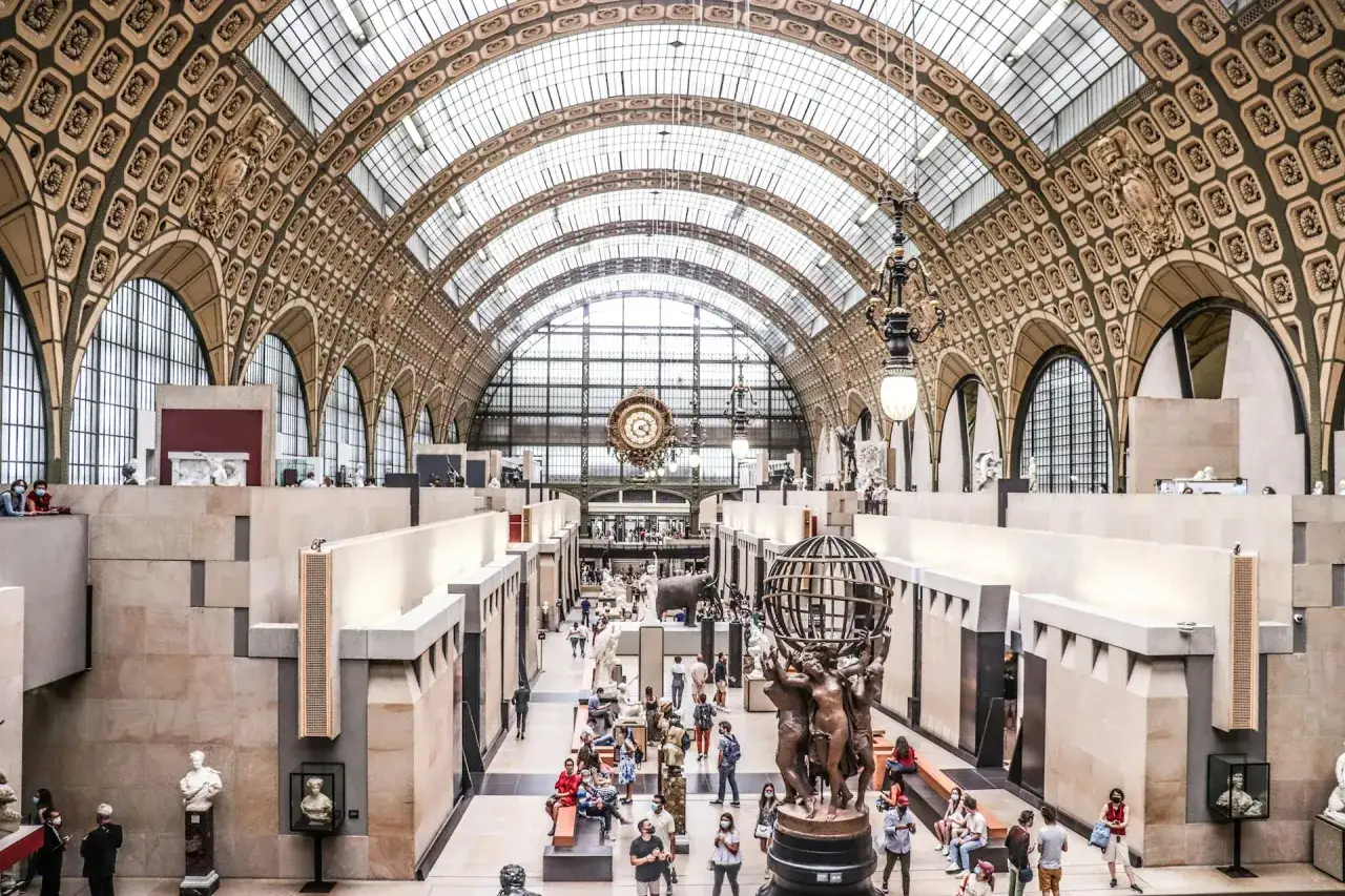 Wnętrze muzeum d'Orsay z rzeźbami i ludźmi zwiedzającymi, pod imponującym, przeszklonym sufitem.