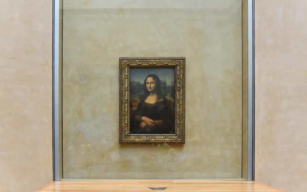 Słynny obraz Mona Lisa w złotej ramie, wiszący na kremowej ścianie. To właśnie tutaj jest Mona Lisa, w Luwrze.