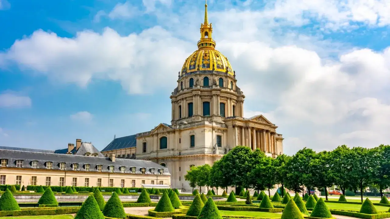 Złota kopuła Les Invalides w Paryżu wznosi się nad zadbanym ogrodem z geometrycznymi żywopłotami.