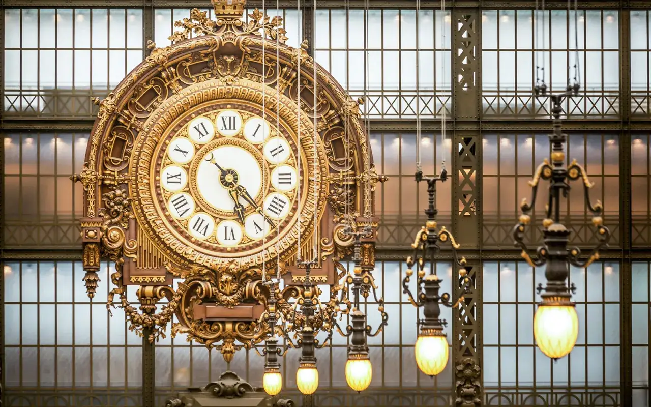 Złoty, zabytkowy zegar w muzeum d'Orsay, ozdobiony rzymskimi cyframi, wisi na tle przeszklonej fasady.