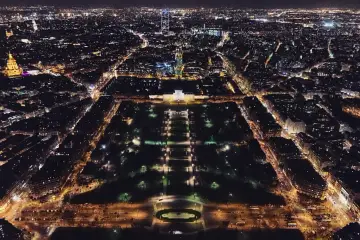 Widok z lotu ptaka na rozświetlone miasto nocą, z widoczną wieżą Eiffla w oddali.